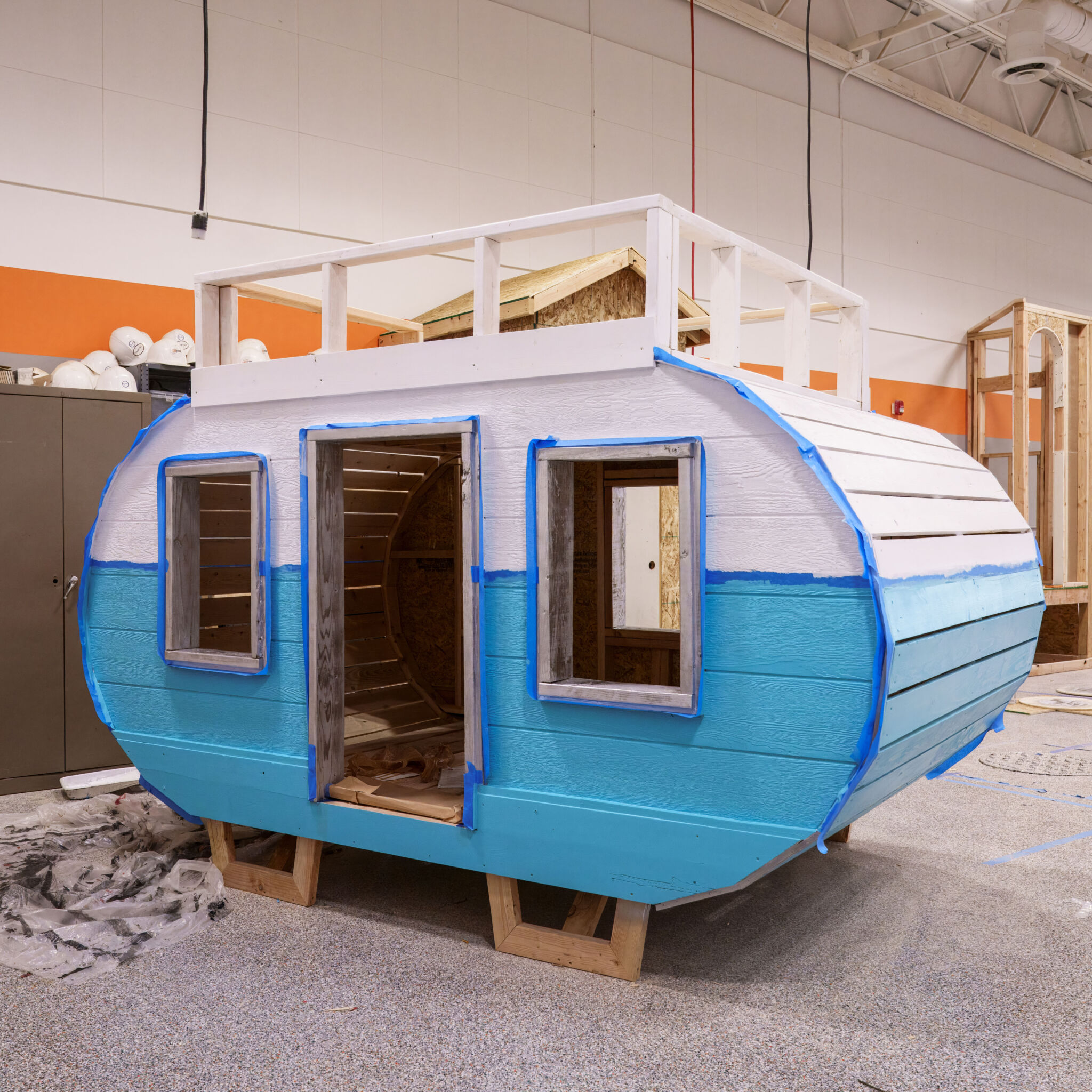 Camper Playhouse A playhouse built to look like a camper, unpainted, sitting in a workshop. There is a balcony at the top.