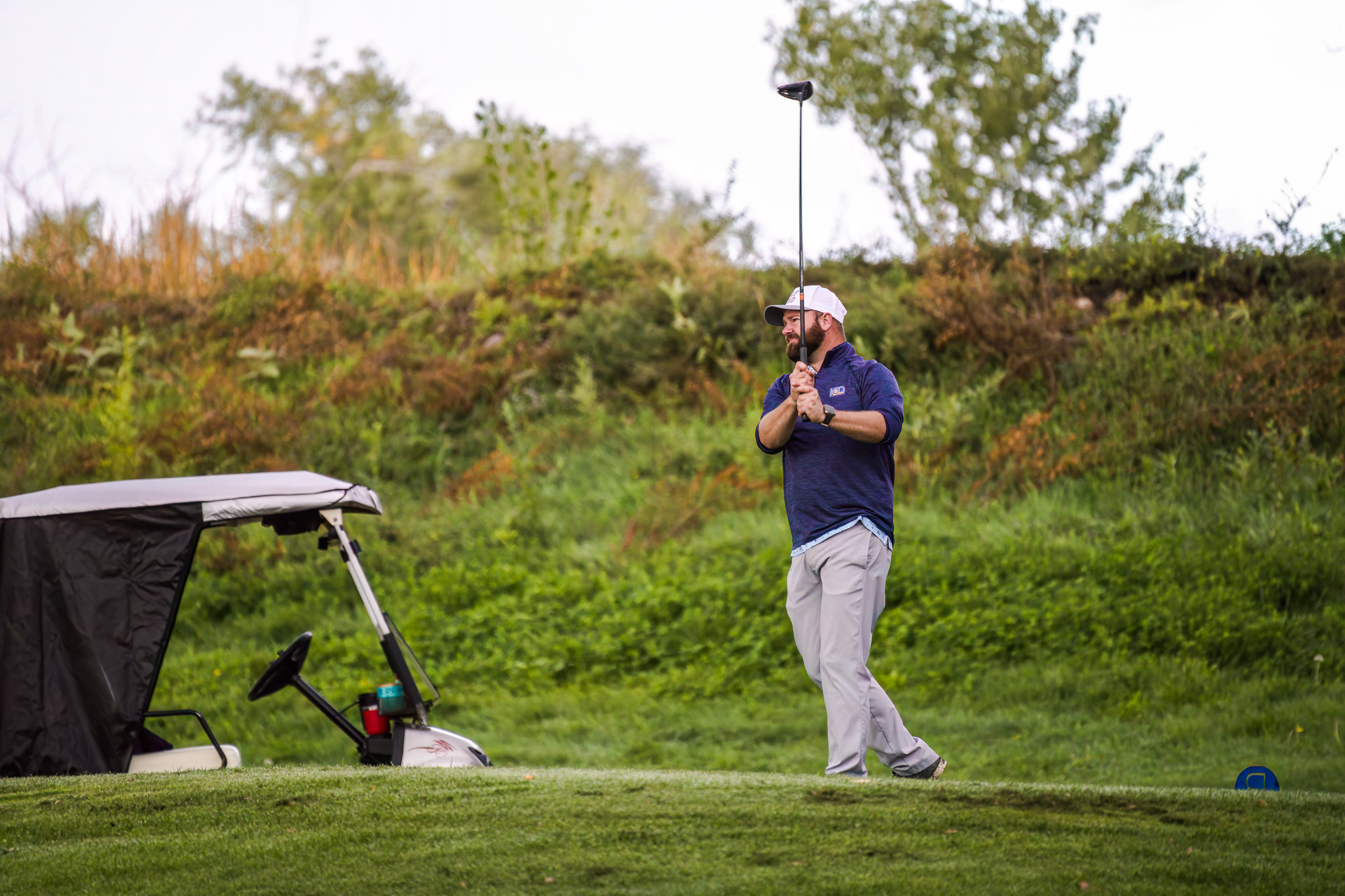 A man ending his golf swing watching his ball