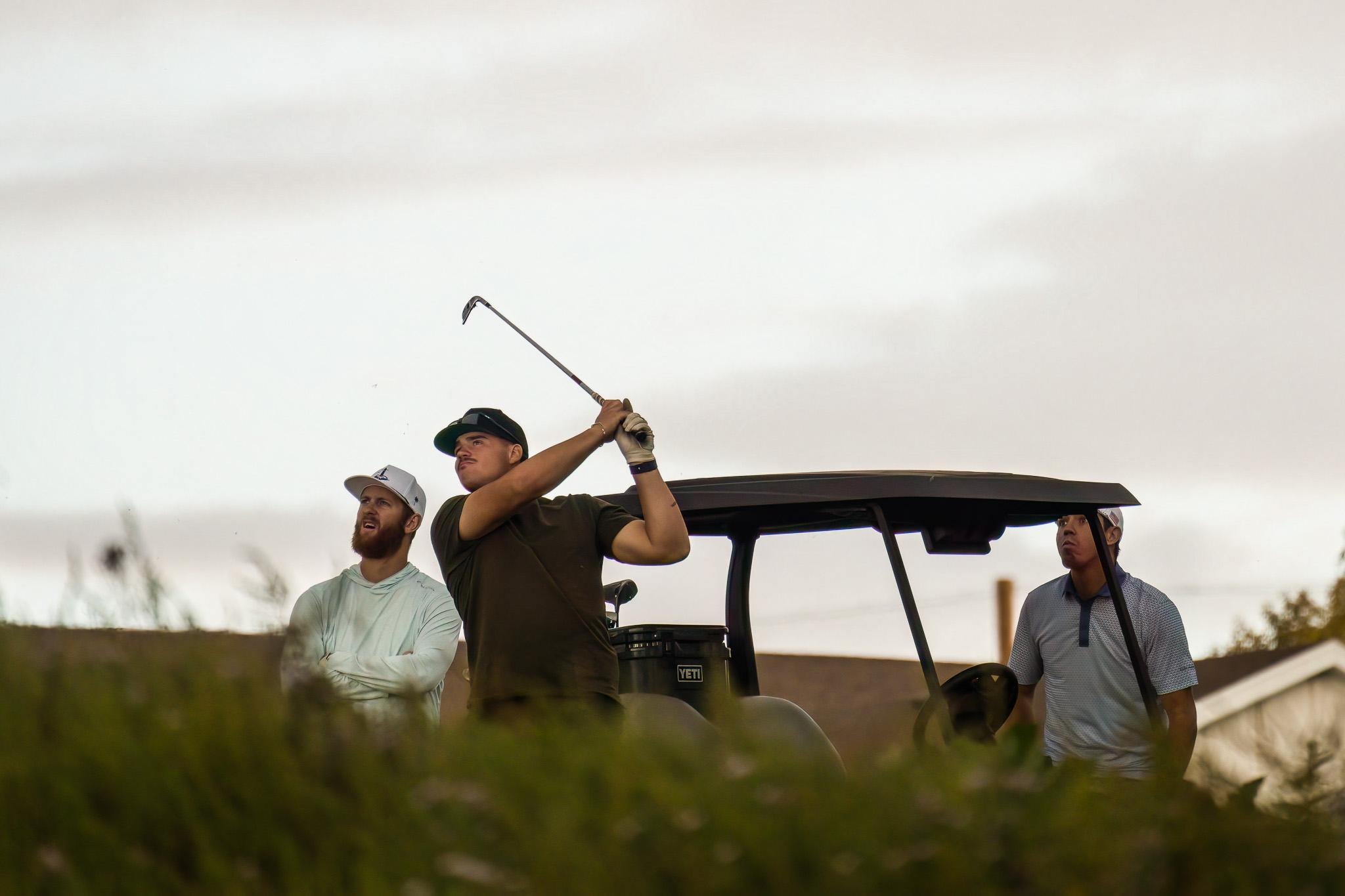 One male golfer finishing his swing with two guys watching the ball