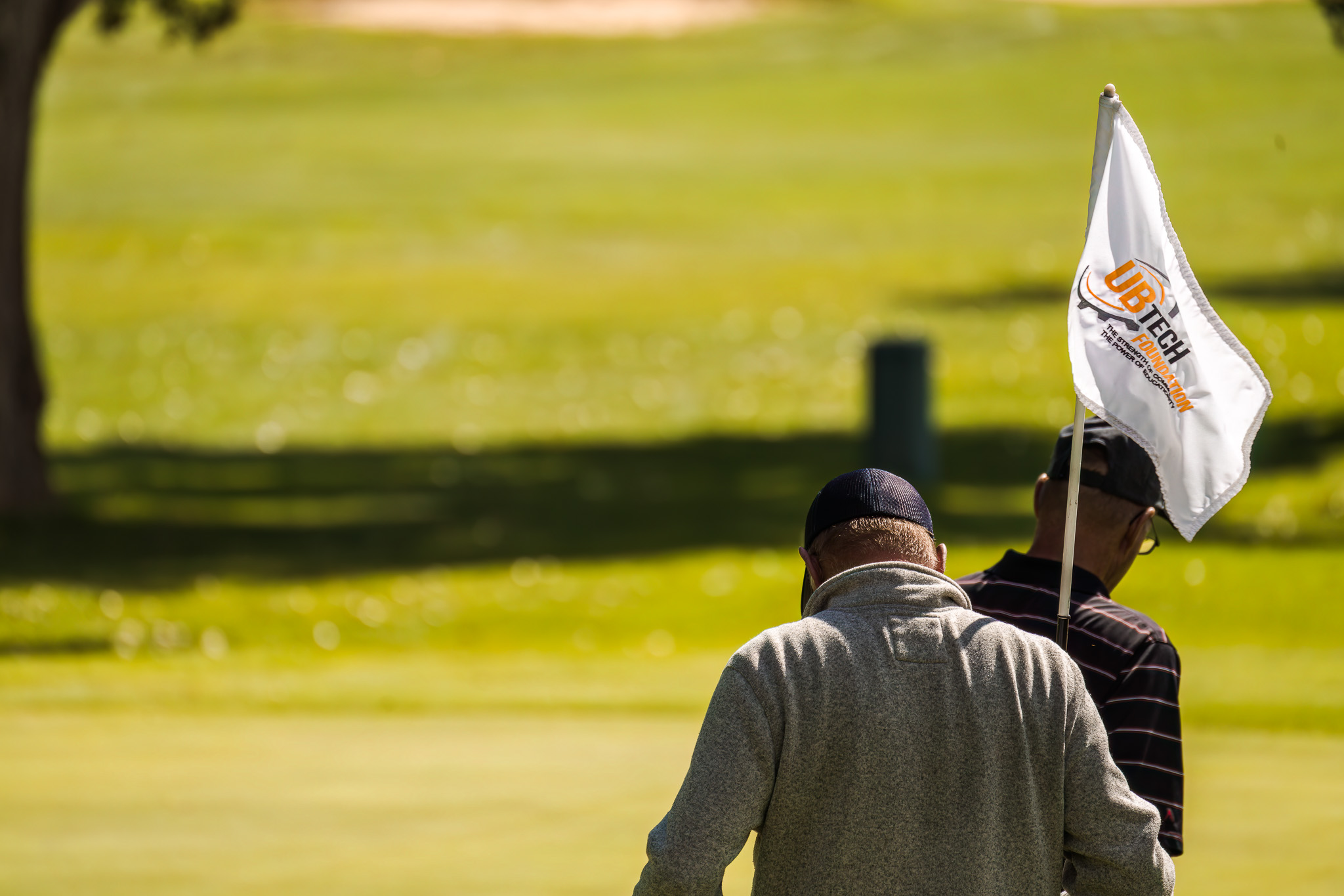 back of a mans head and shoulders as he is putting the golf flag back in the hole and the flag reads UBTech Foundation