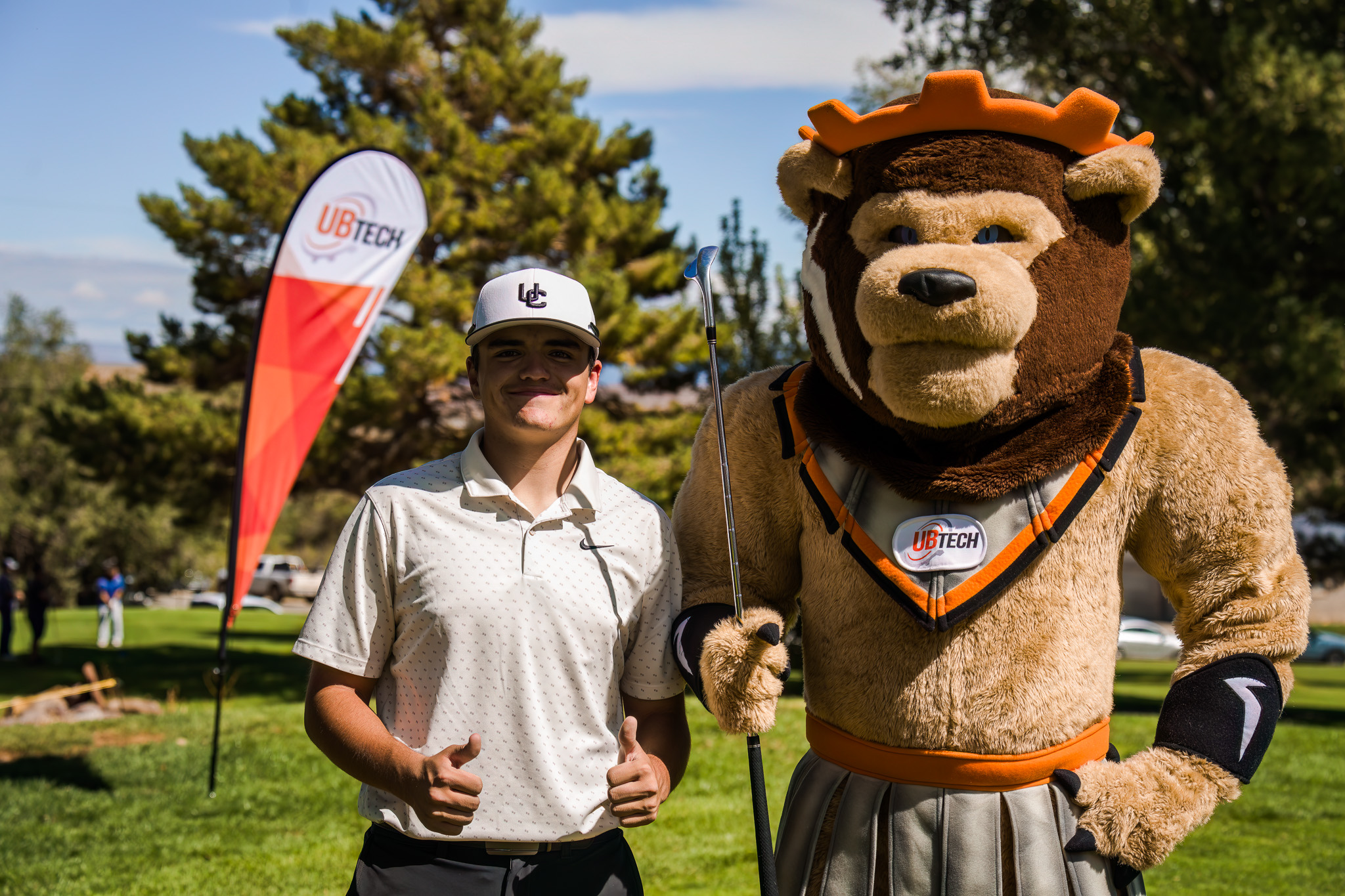 A male standing next to and posing with the lion mascot