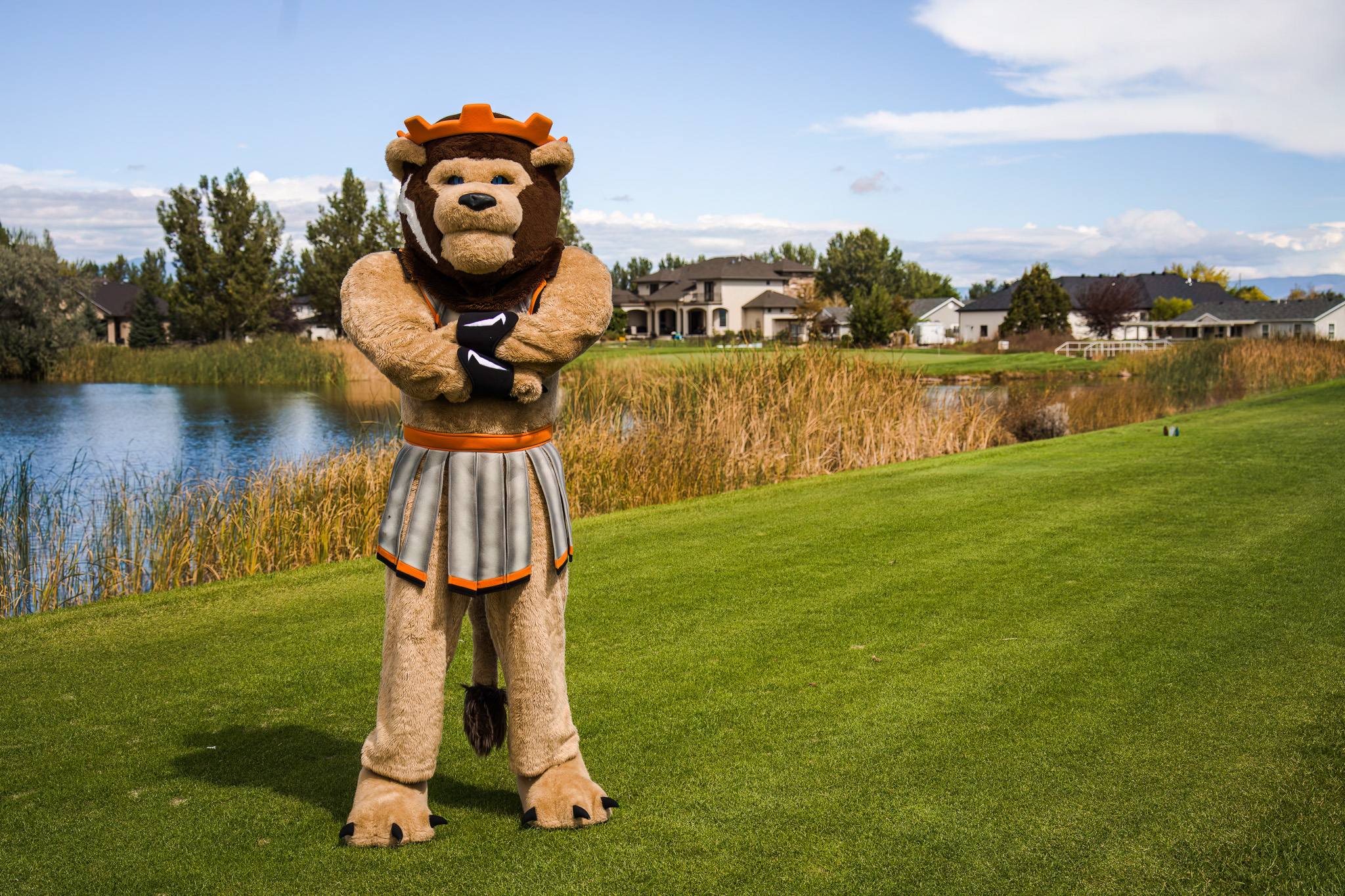 Lion Mascot standing arms crossed in front of a pond golf hole