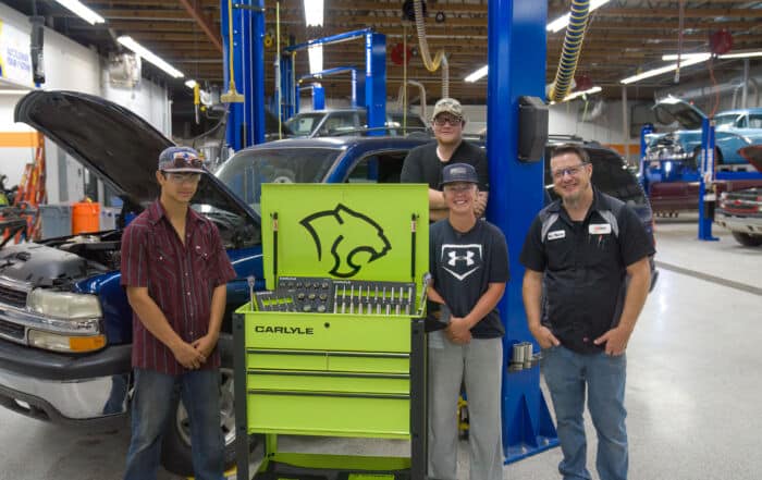 Three students and a instructor stand around a bright lime green Carlyle toolbox in front of a blue suburban smiling for the camera.