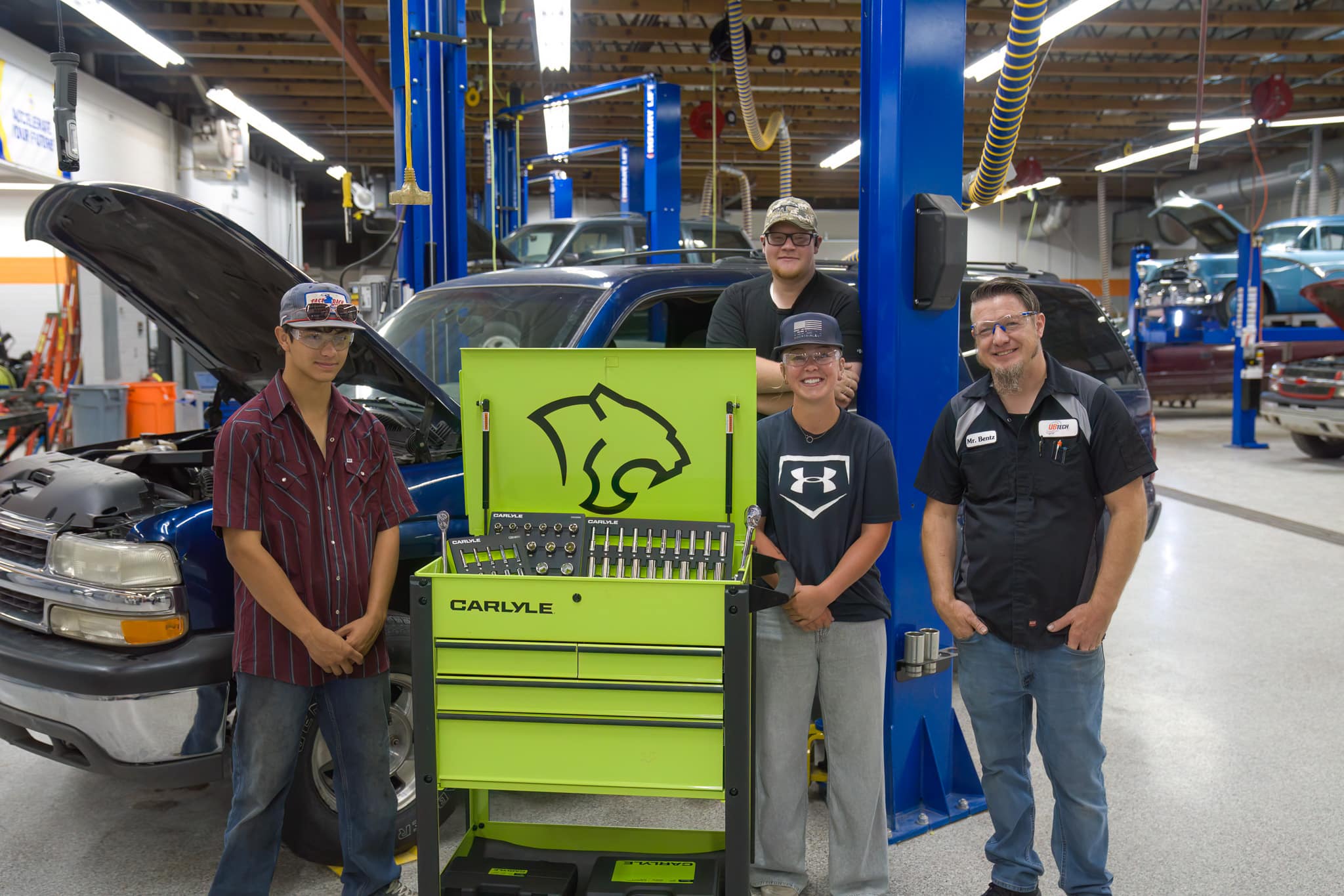 Three students and a instructor stand around a bright lime green Carlyle toolbox in front of a blue suburban smiling for the camera.
